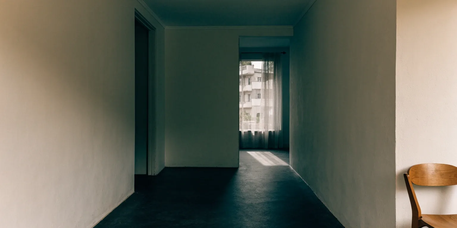 Overcast light spilling from a doorway across a charcoal floor in a quiet studio building