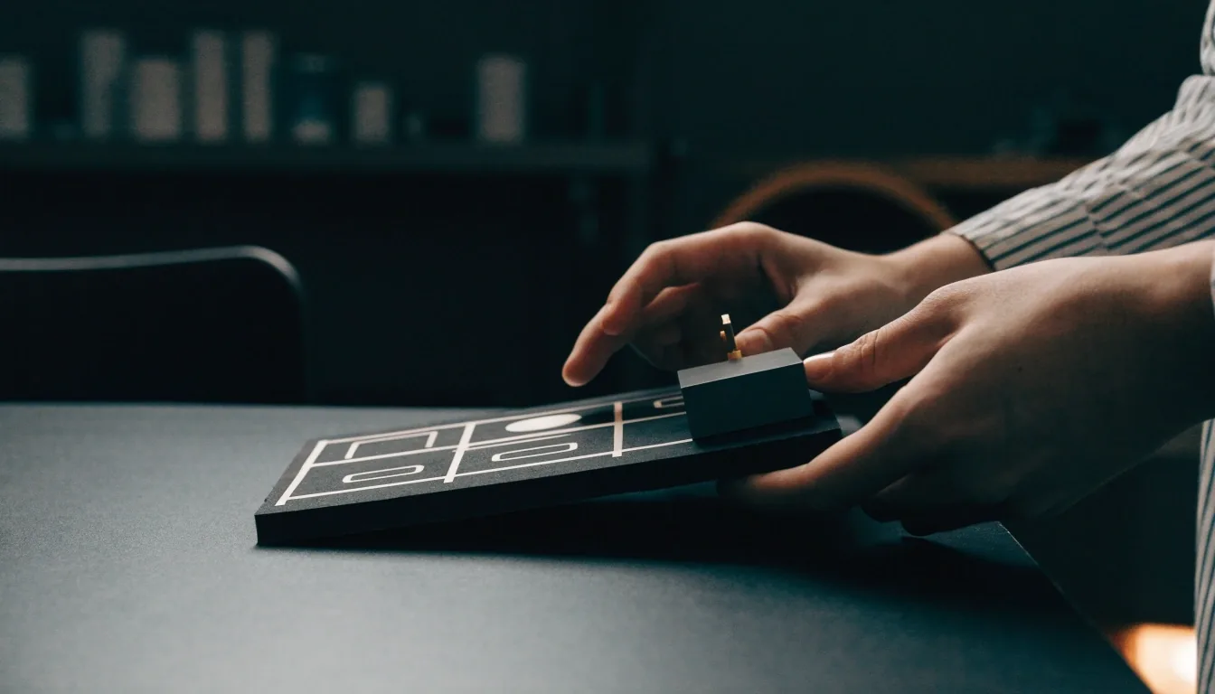 A hand placing a small matte object onto a dark felt tabletop, the rest of the scene still